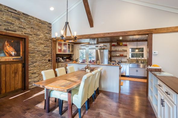 Rustic kitchen with a long dining table, stone accent wall, and wooden beams.