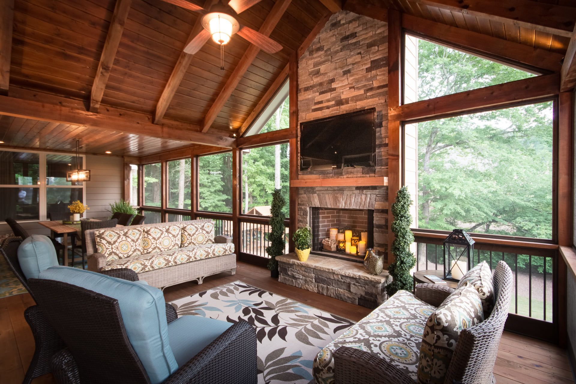Screened-in porch with fireplace, TV, and seating, offering a view of the surrounding nature.
