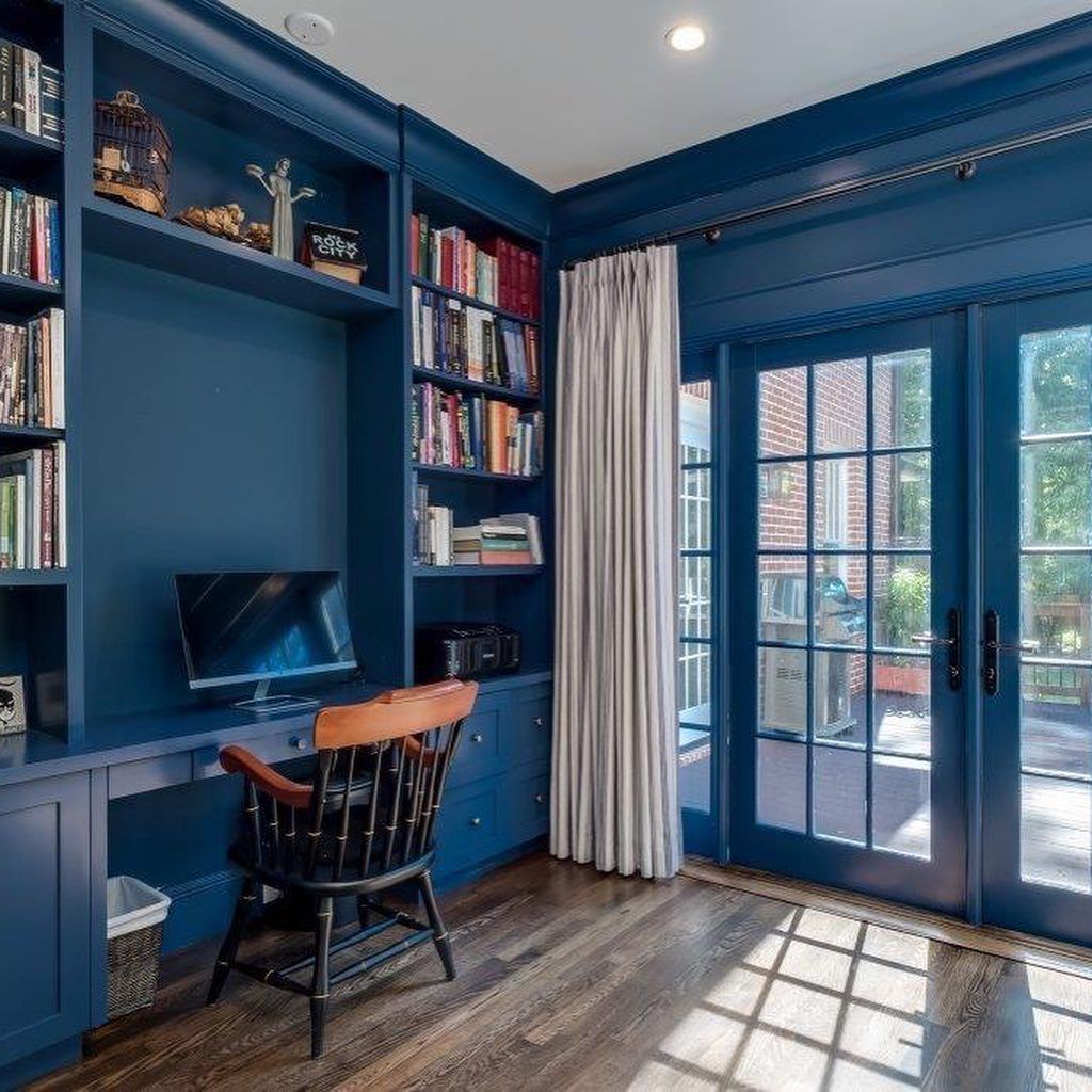 Blue home office with built-in shelves, desk, and French doors. A dark wood desk chair sits in front of the desk.