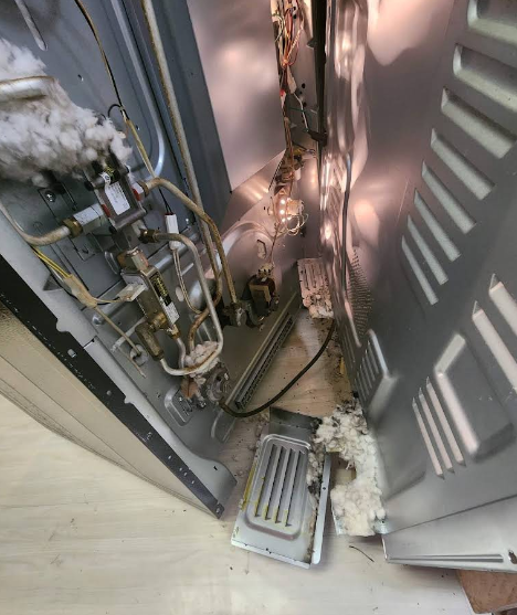 Damaged oven interior, showing exposed wiring, insulation, and a fallen metal panel.