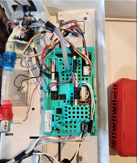 Open circuit board with colorful wires and components inside a white cabinet, next to a red box.