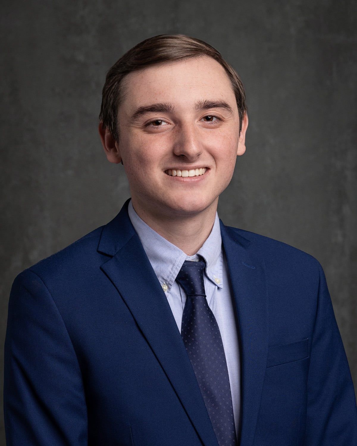 A young man in a blue suit and tie is smiling for the camera.