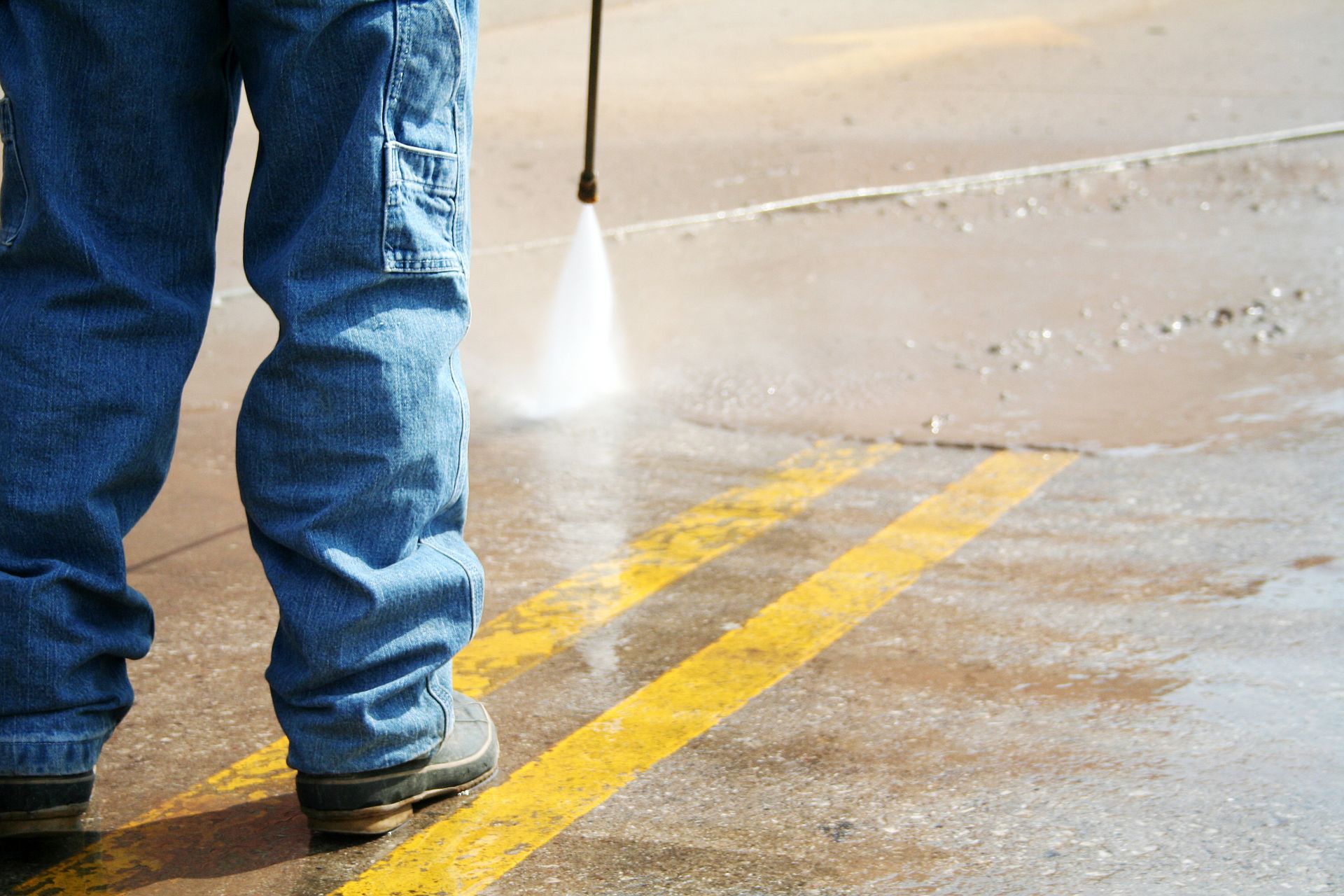 Person in jeans power washing yellow road lines.