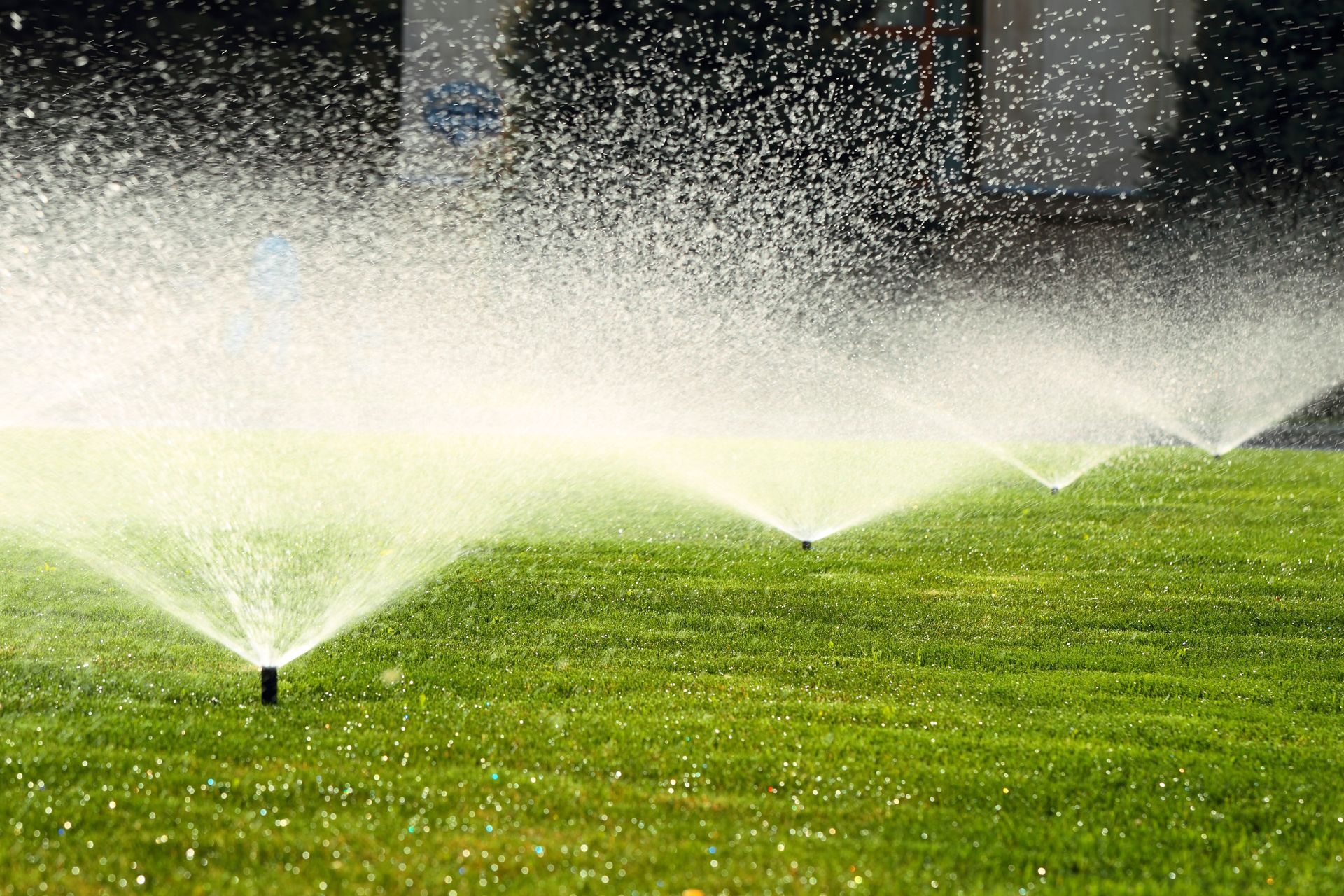 Sprinklers spraying water on a green lawn, creating a mist in the air.