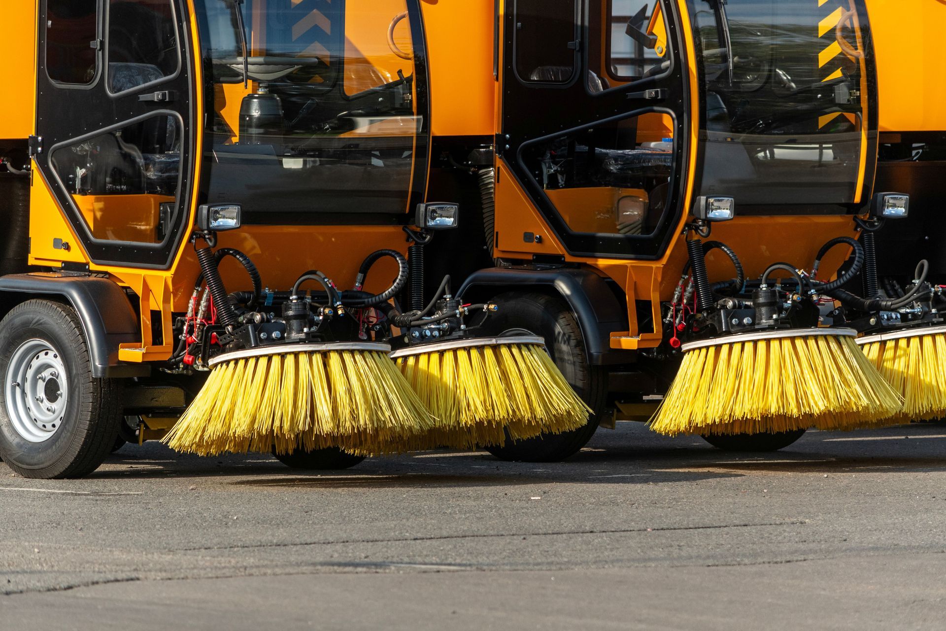 Yellow street sweepers with large circular brushes parked outdoors.