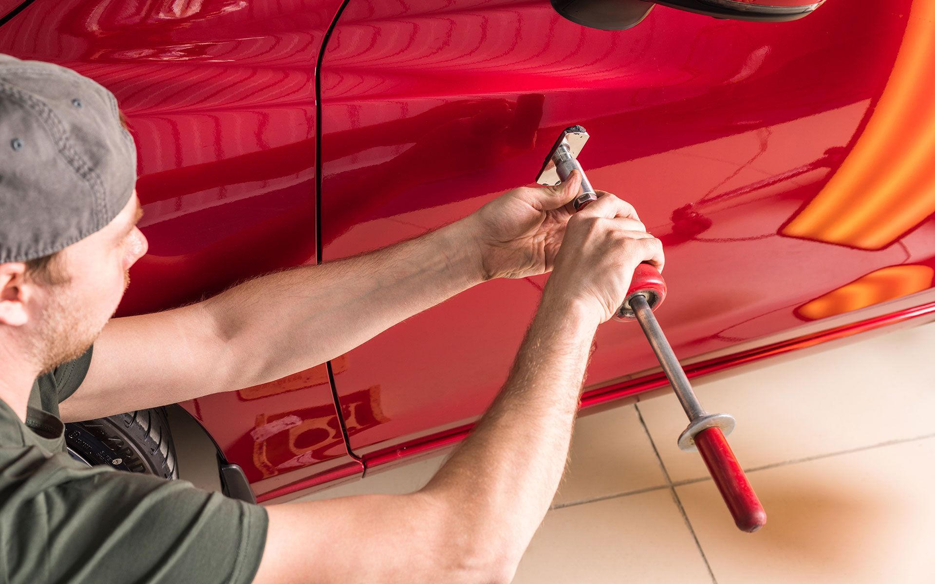 A person is using a dent removal tool on the red side of a car.