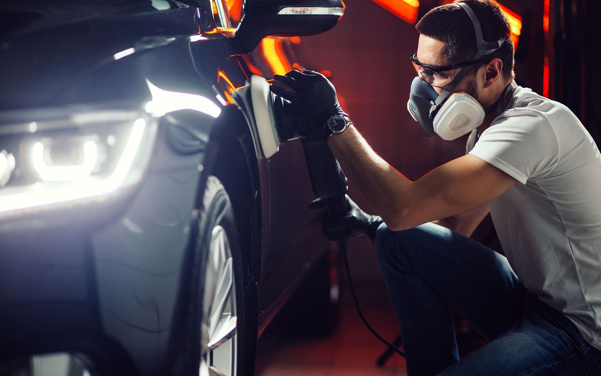 Person polishing a car with a machine, wearing protective gear like a mask and gloves.