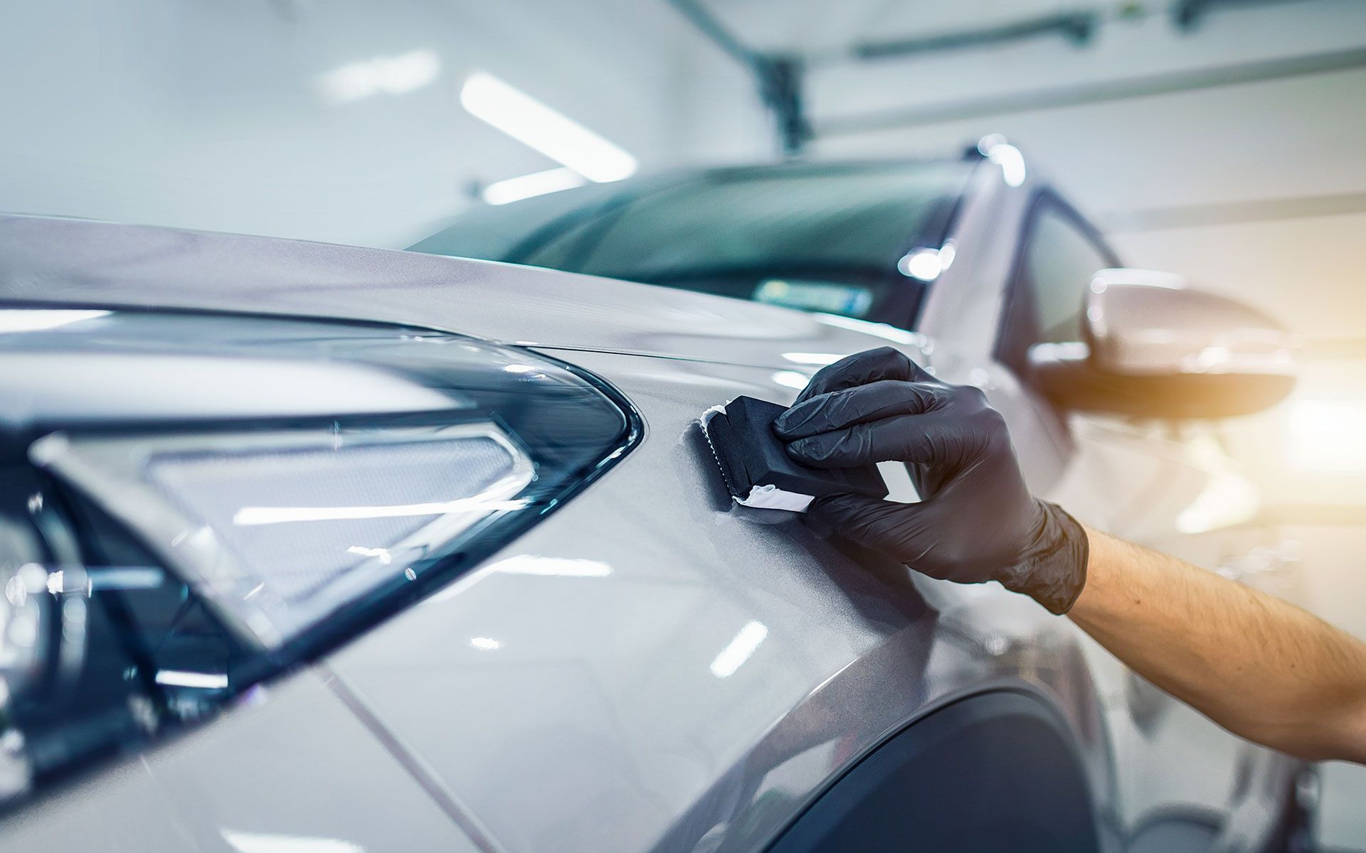 Person applying ceramic coating to a car with black-gloved hand in a garage.