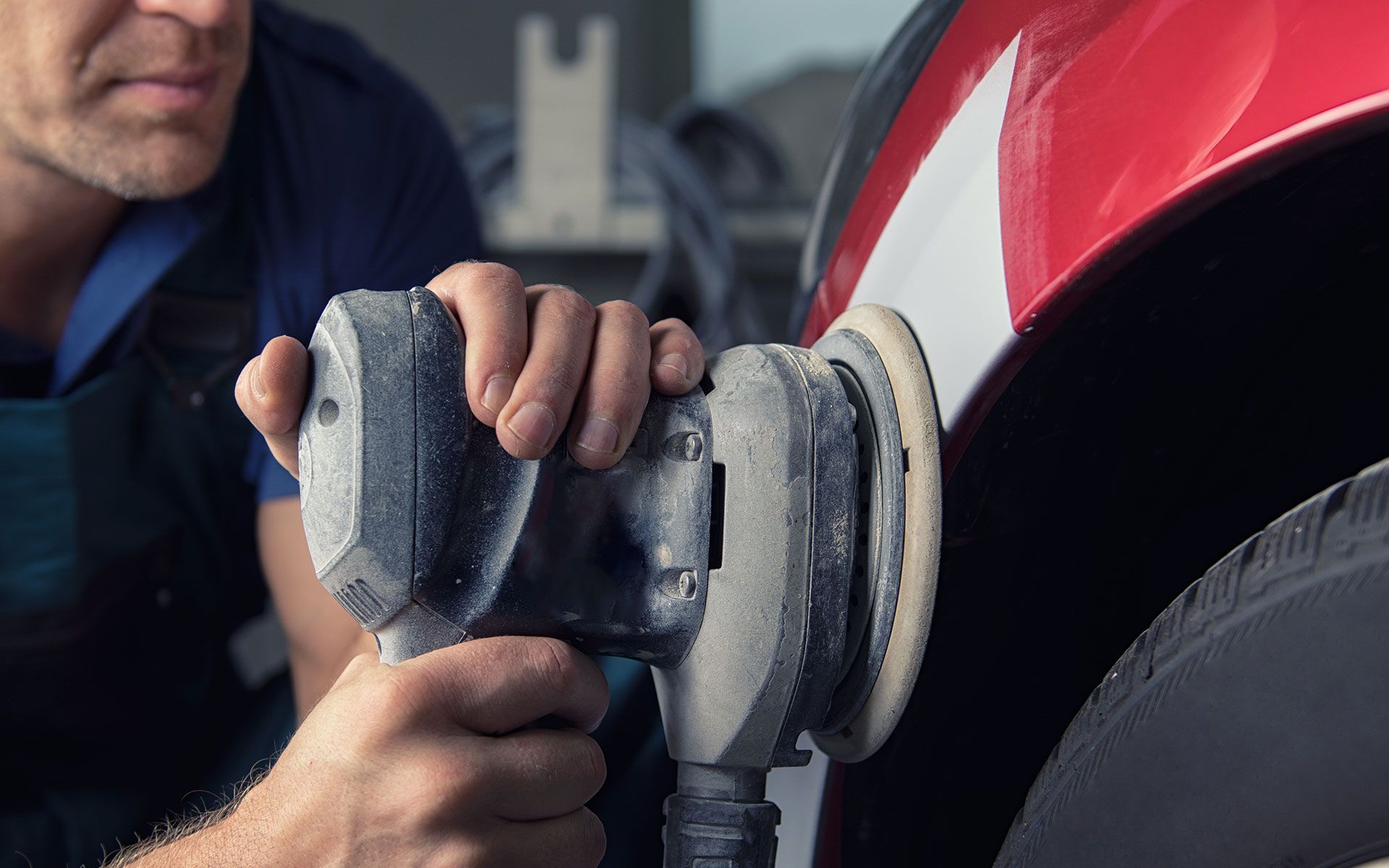 Person sanding red car panel with a power sander.