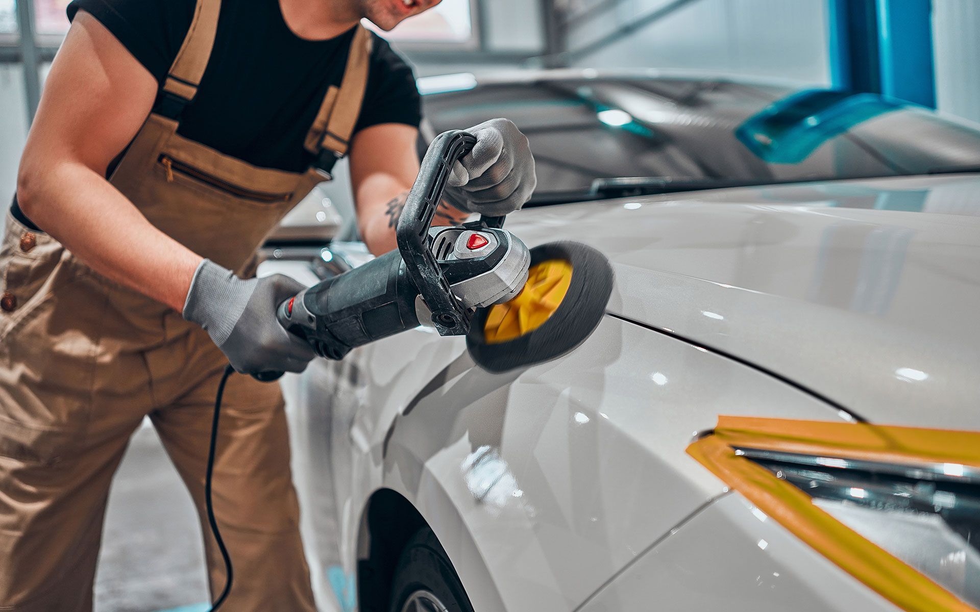 Mechanic buffing a white car with a power tool in a garage.