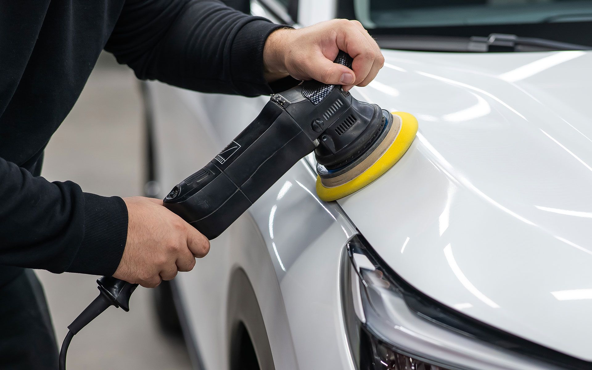 Person polishing a white car with a power buffer.