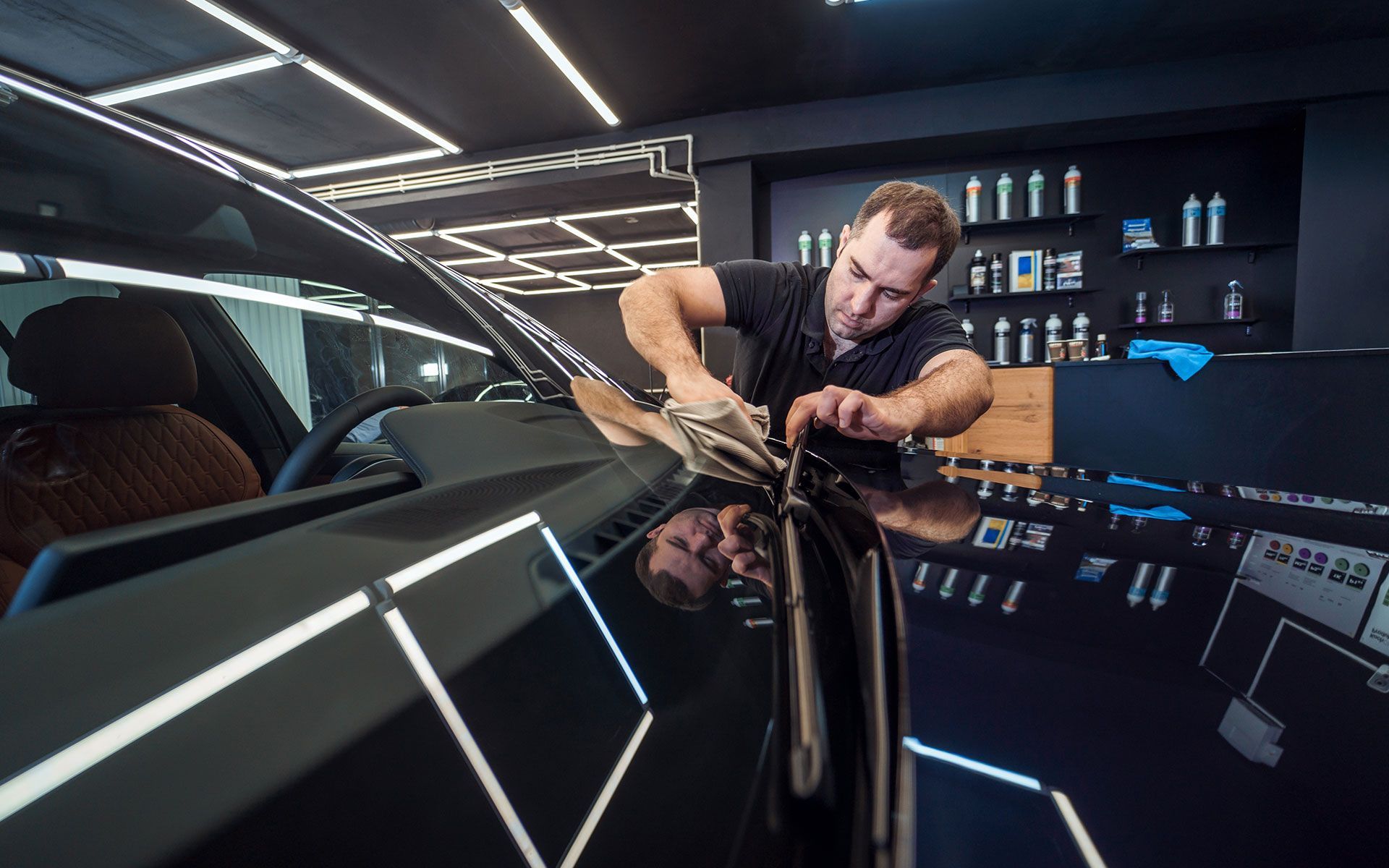 A man applying film to a black car's hood in a professional shop.