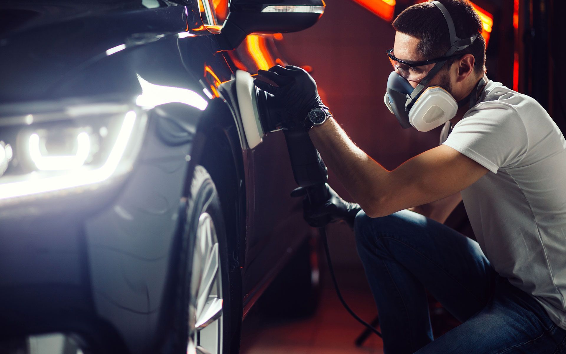 Man polishing car with electric buffer, wearing safety glasses, mask, and gloves.