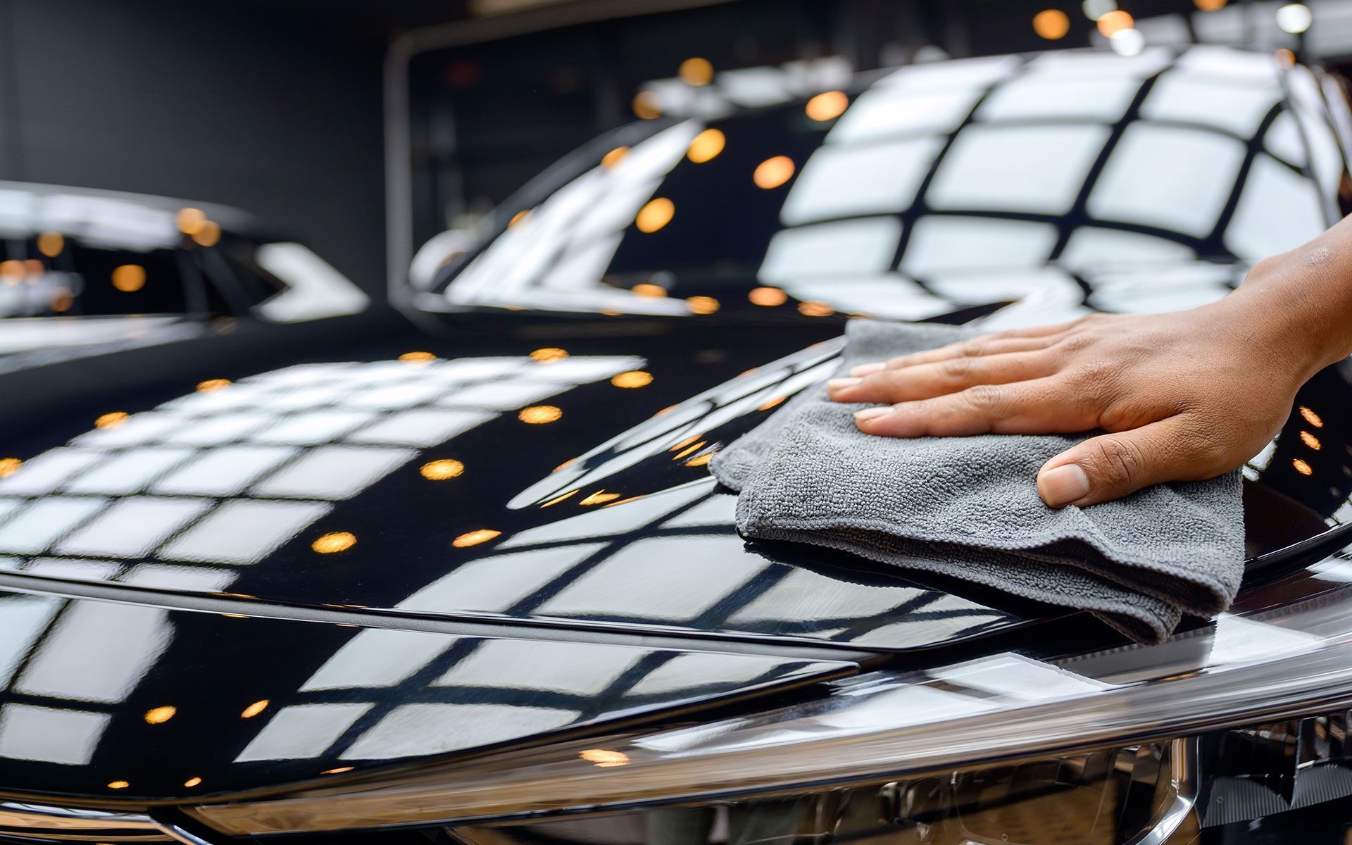 Hand wiping a shiny black car with a gray microfiber cloth.