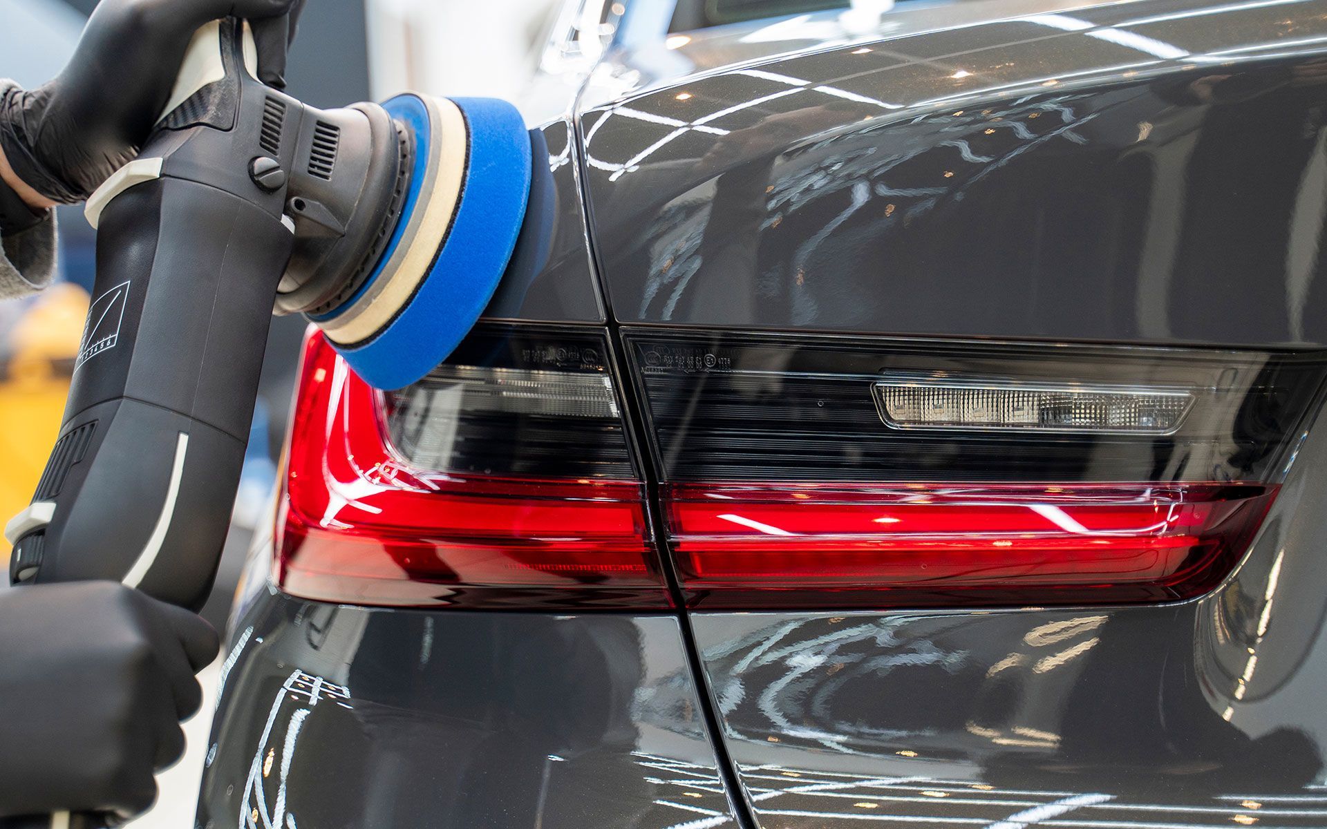 Detailing a dark gray car with a polishing machine.