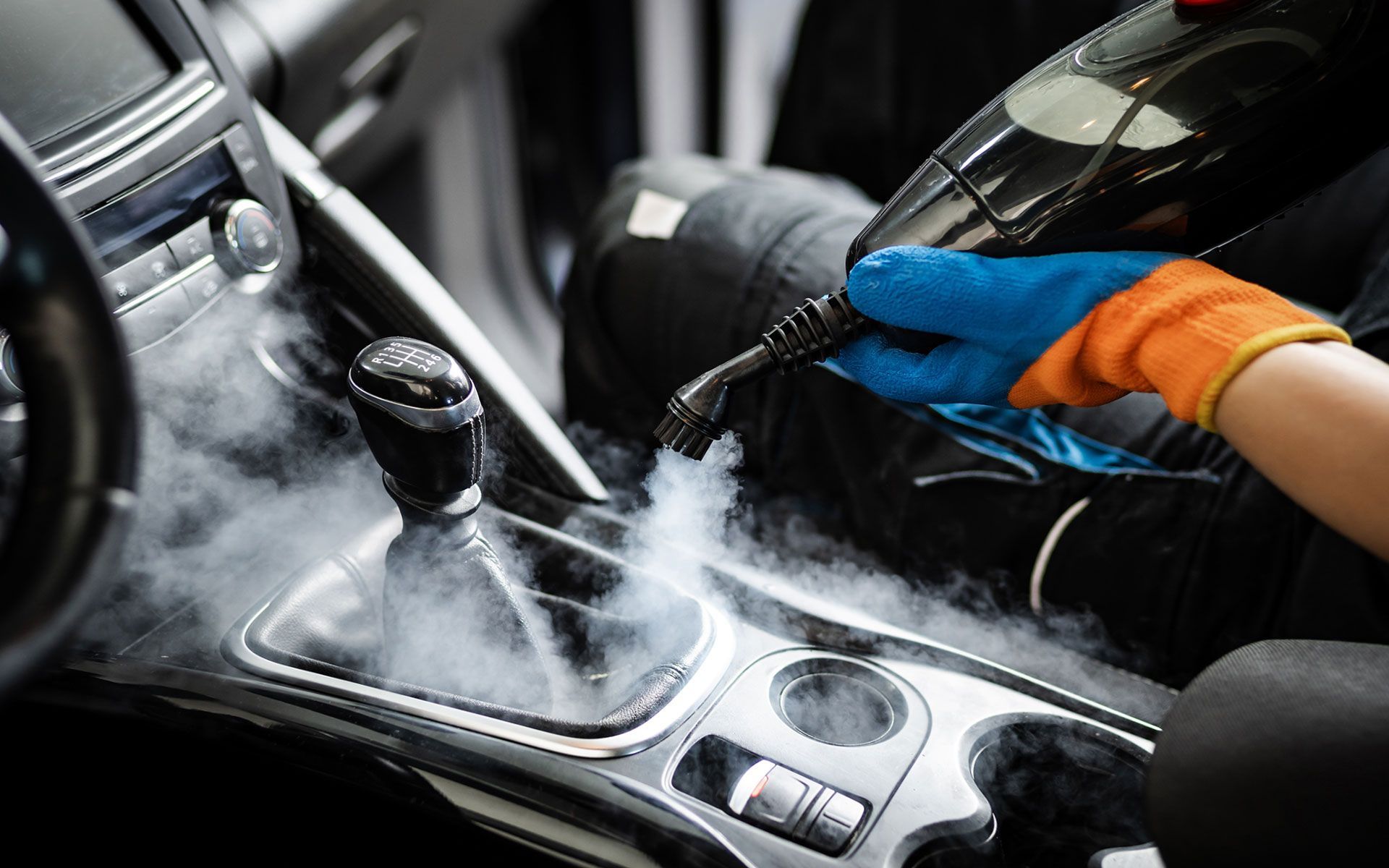 Person steam cleaning a car interior with a handheld device, emitting steam on the console.