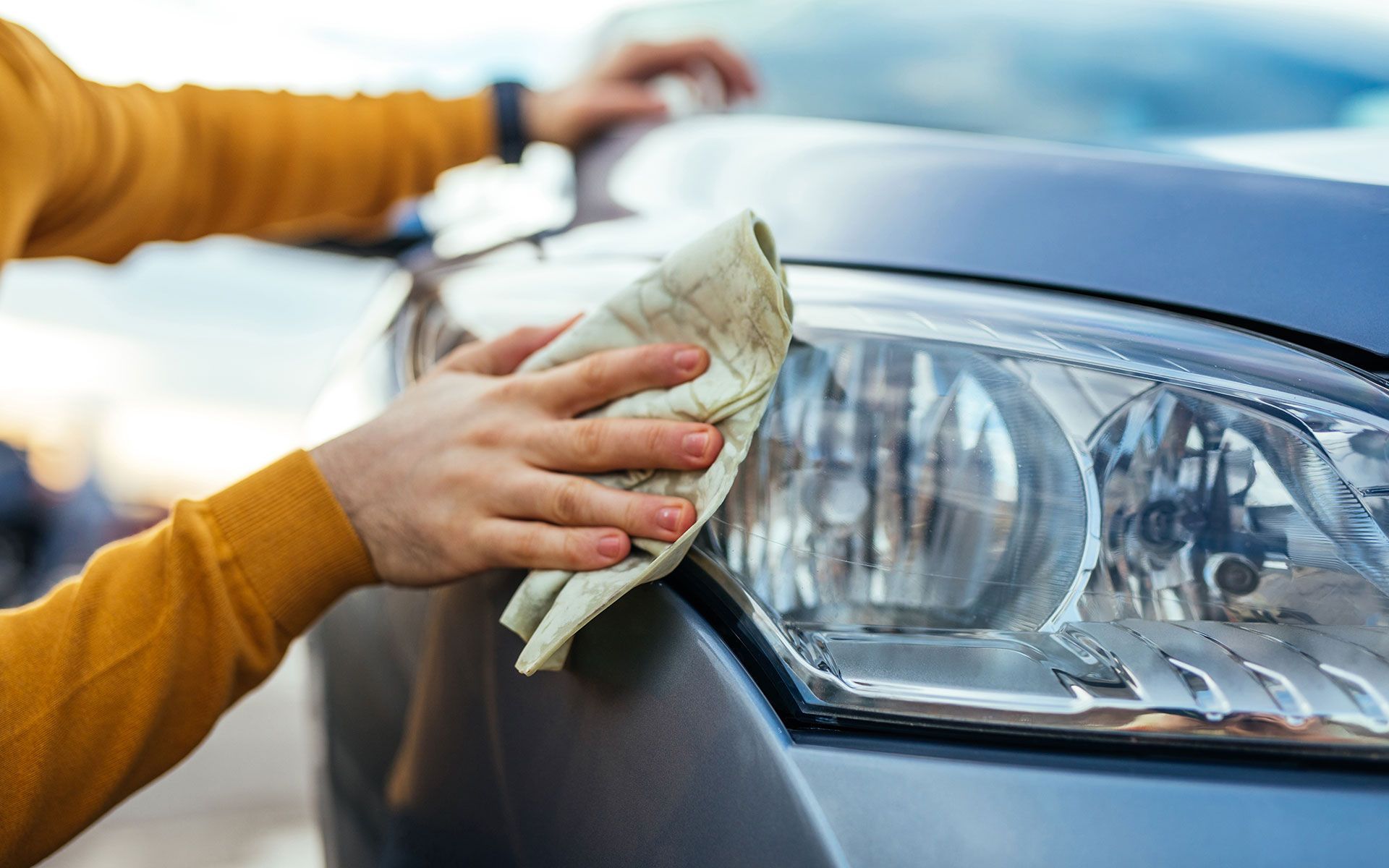 Person in yellow sweater cleaning a car headlight with a cloth.