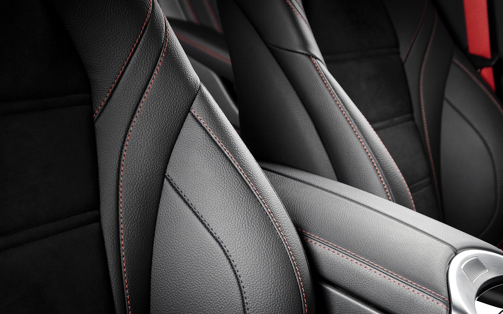 Close-up of a black car seat with red stitching, highlighting the textures and design details.