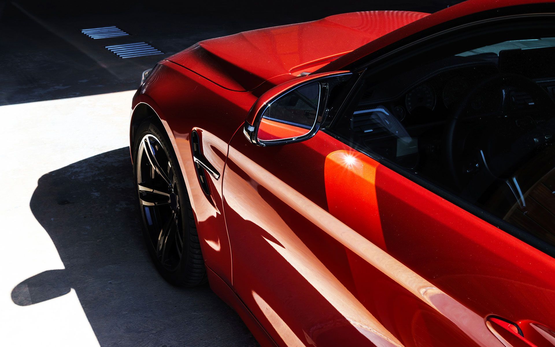 Red sports car, partially shown, parked on a gray surface with sunlight casting shadows.