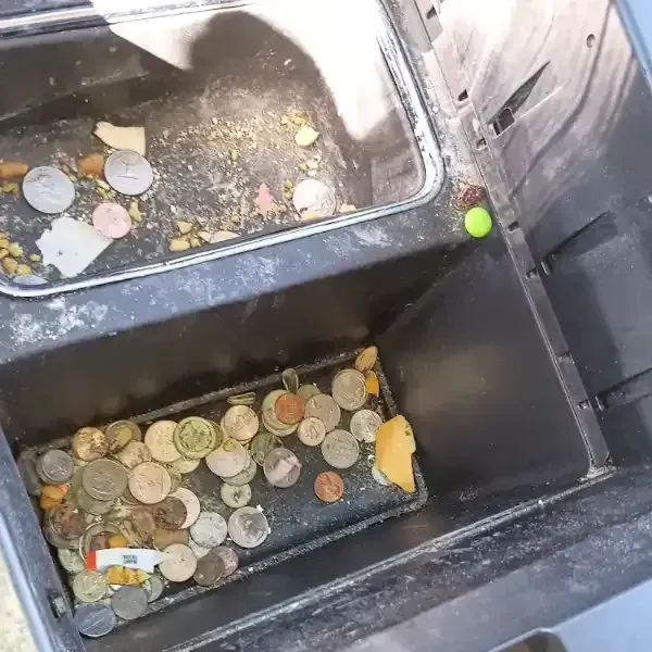 Open, dirty coin dispenser with coins and debris.