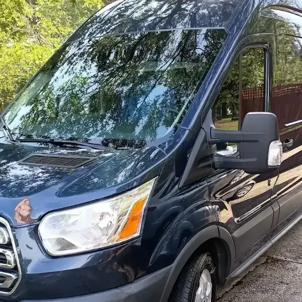 Dark blue van parked outdoors, reflecting trees. Headlight visible.