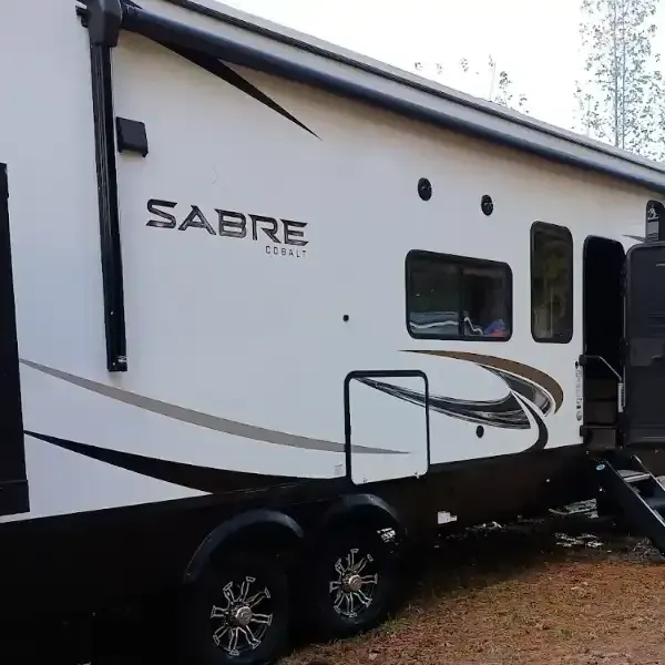 White and brown Sabre Cobalt RV with black accents, parked outdoors, steps visible.