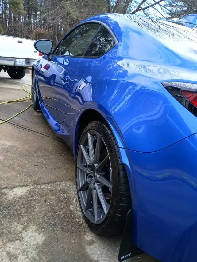 Blue sports car, rear quarter view, parked on concrete. Silver wheels, black mud flap.
