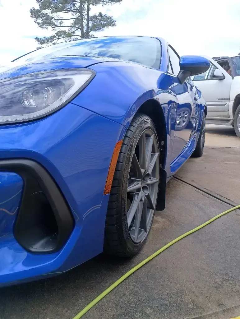 Blue sports car parked outside, close-up of the front, with a yellow hose in the foreground.