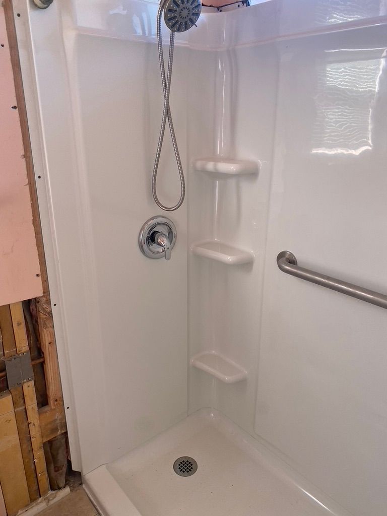 White shower stall with shelves and a grab bar, under construction.
