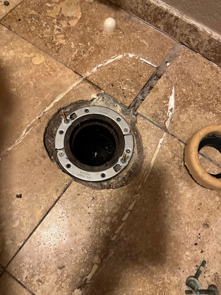 Toilet flange on tiled floor, with old wax ring nearby.