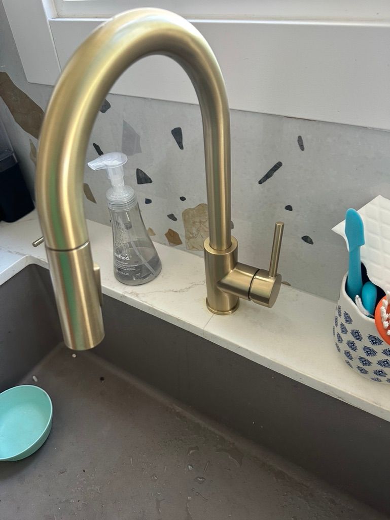 Gold kitchen faucet with a pull-down sprayer, set against a speckled backsplash.