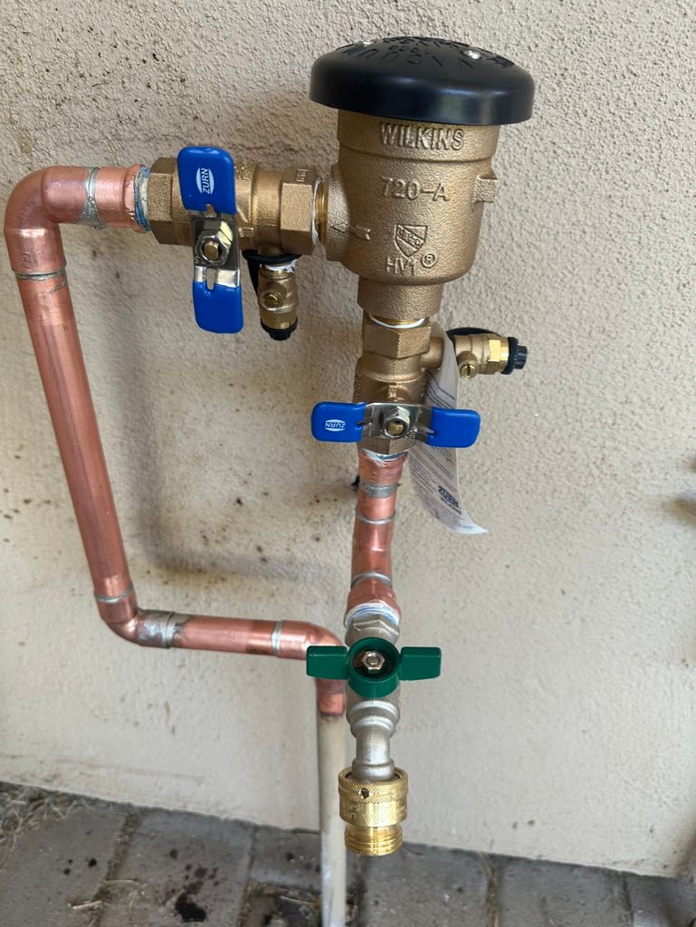 Copper pipes and valves connect to a water backflow preventer against a textured wall.