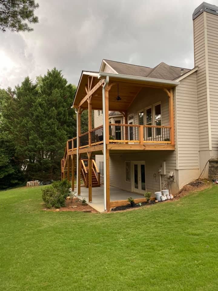 Two-story wooden deck attached to a beige house with a covered upper level and stairs to the yard.