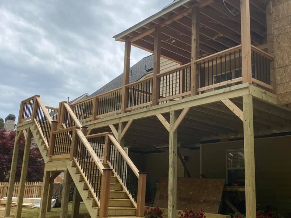 Wooden deck with stairs, railings, and covered upper level attached to a house under a cloudy sky.