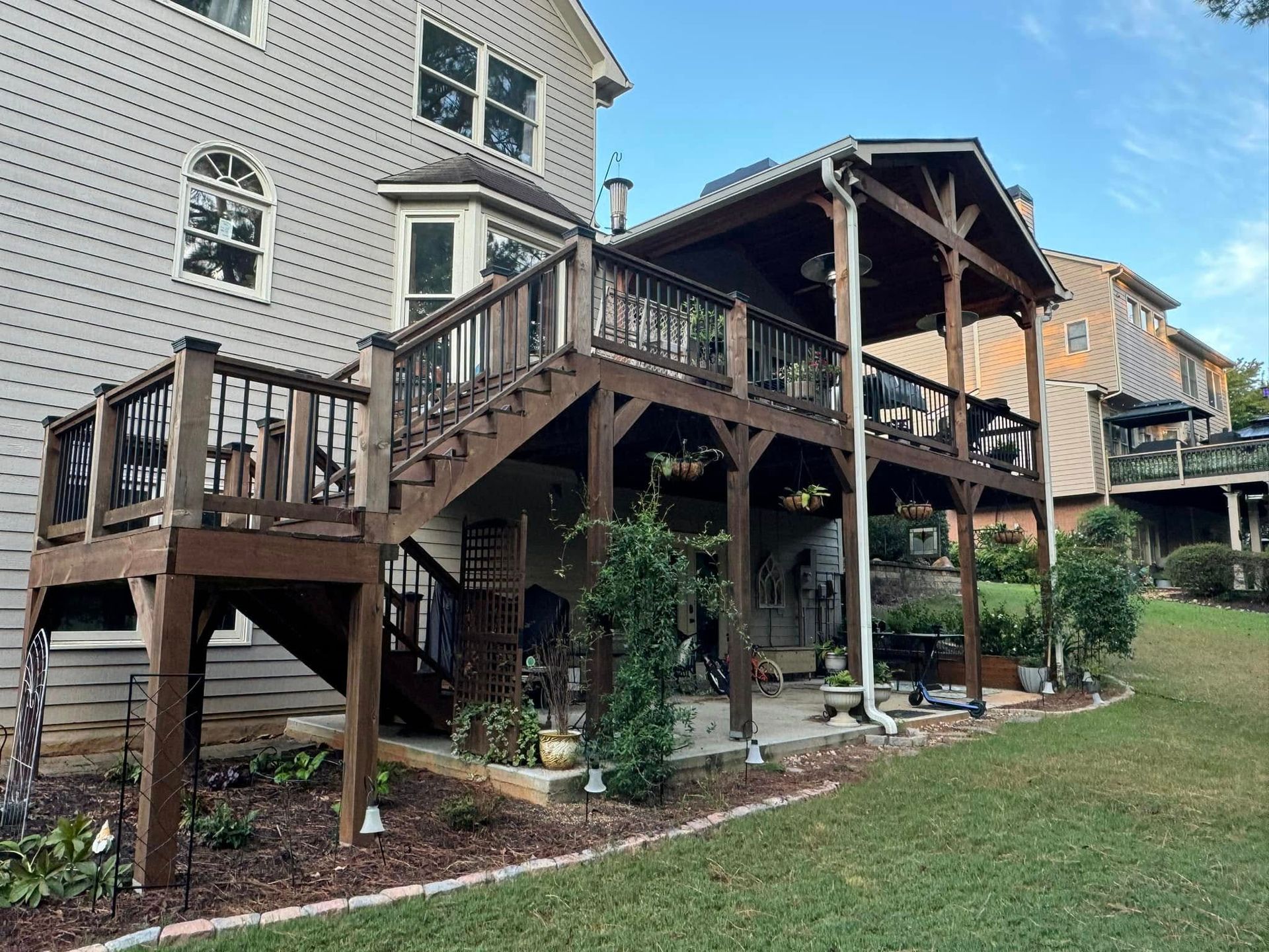 Brown wooden deck attached to a house, with a covered area and stairs leading down to a backyard.
