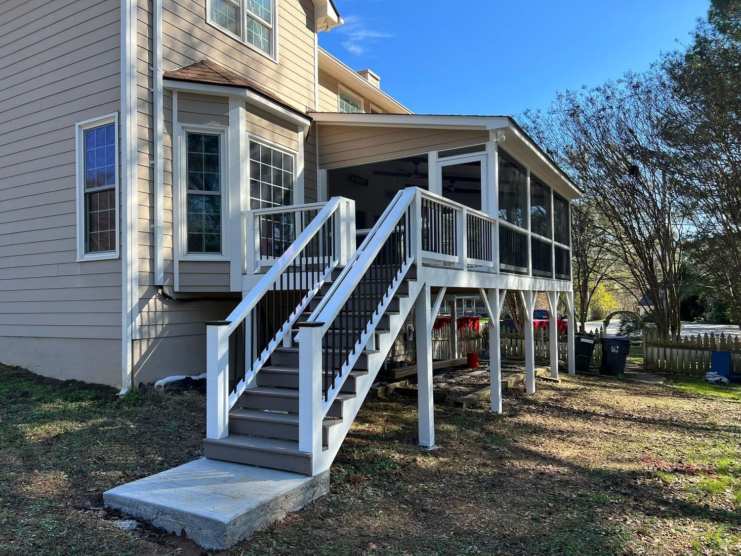 Exterior of a house with a screened porch and stairs. White railings, black balusters, gray concrete steps.