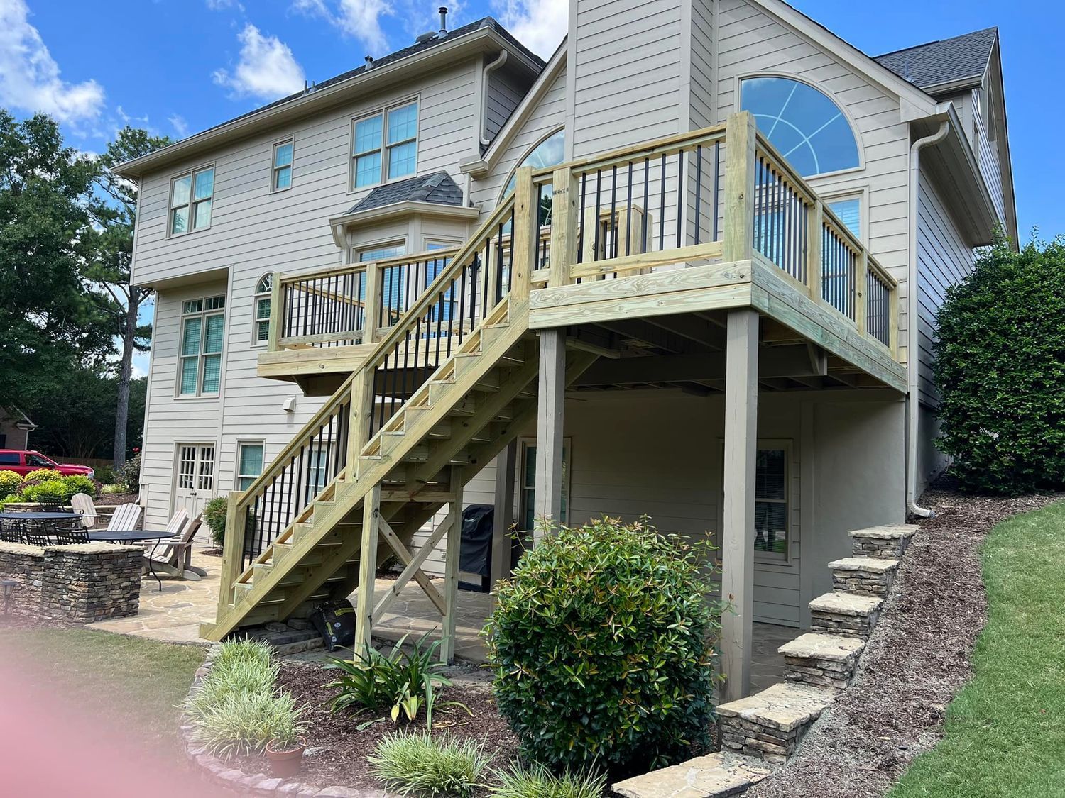 Two-story wooden deck on the back of a house, with stairs leading down to the ground and a patio area.