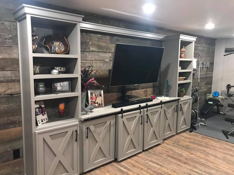 Gray entertainment center with barn-style doors, shelves, and TV on a wooden accent wall.
