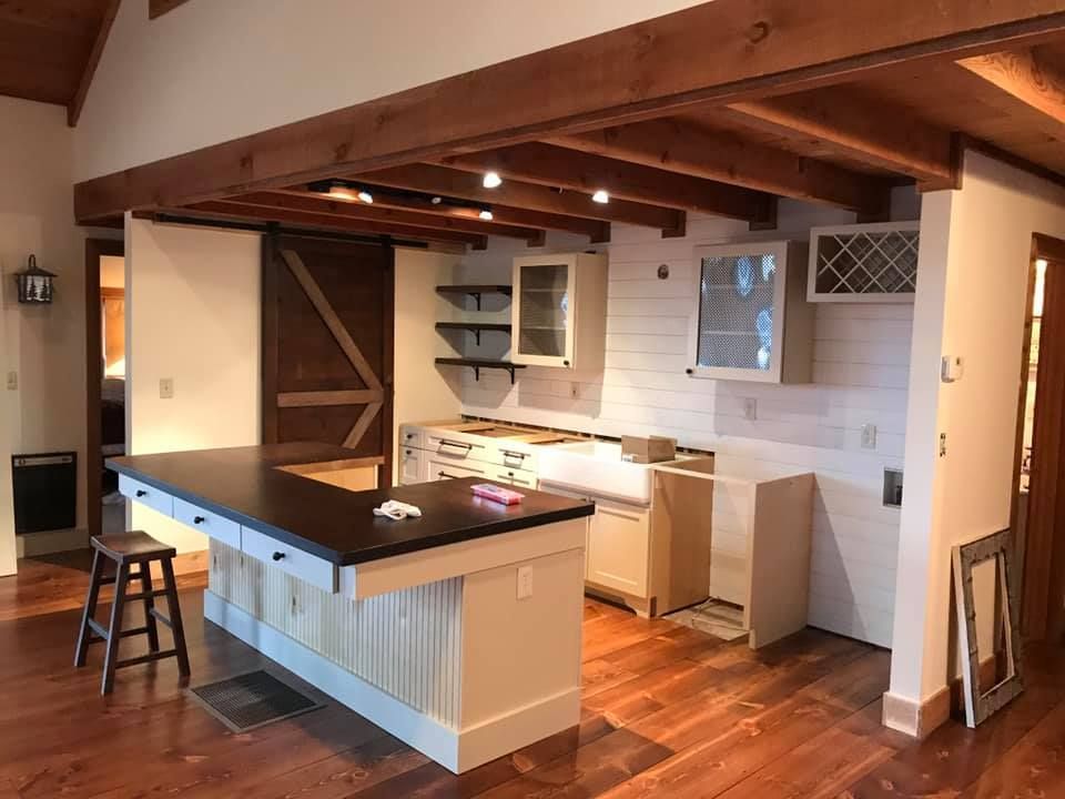 Kitchen renovation: island with black countertop, cabinets, wood floors and beams.