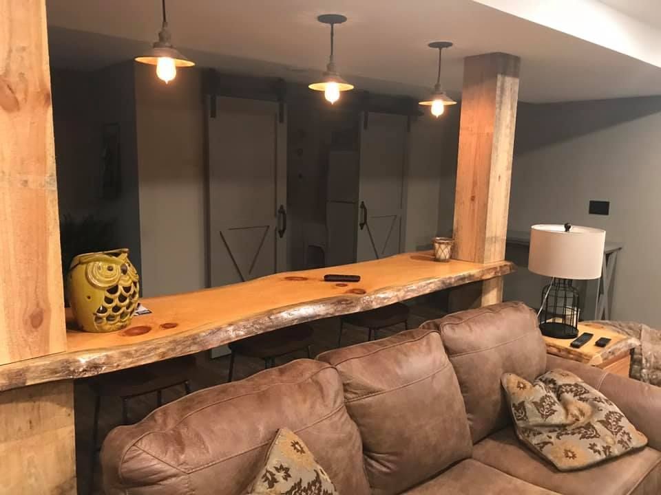 Cozy basement bar with live-edge wood counter, pendant lights, and brown leather couch.