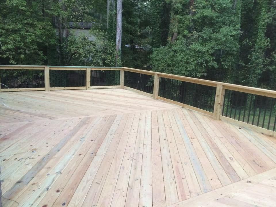 Wooden deck with black railing, surrounded by trees.