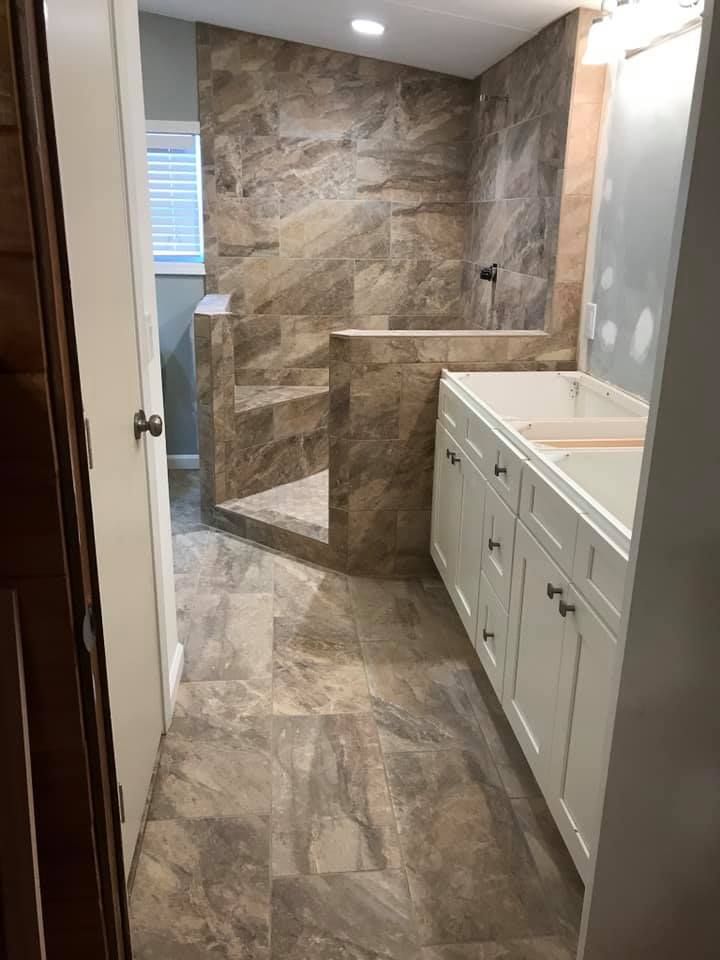Bathroom renovation: tiled shower with steps, white vanity, and brown floor tiles.