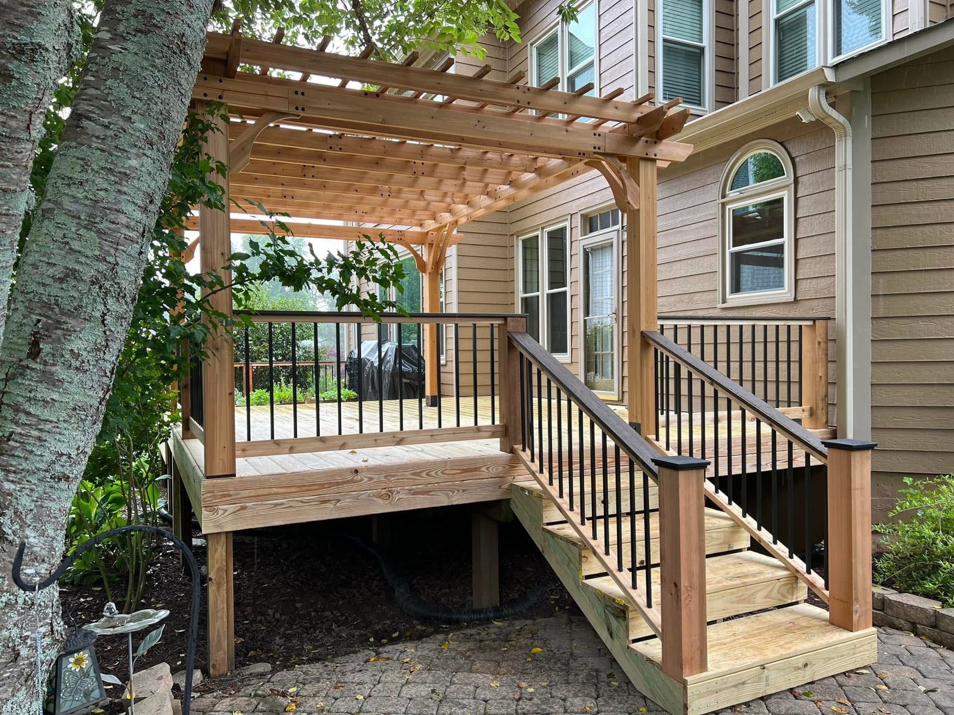 Wooden deck with pergola, stairs, and black railings leading to a house.