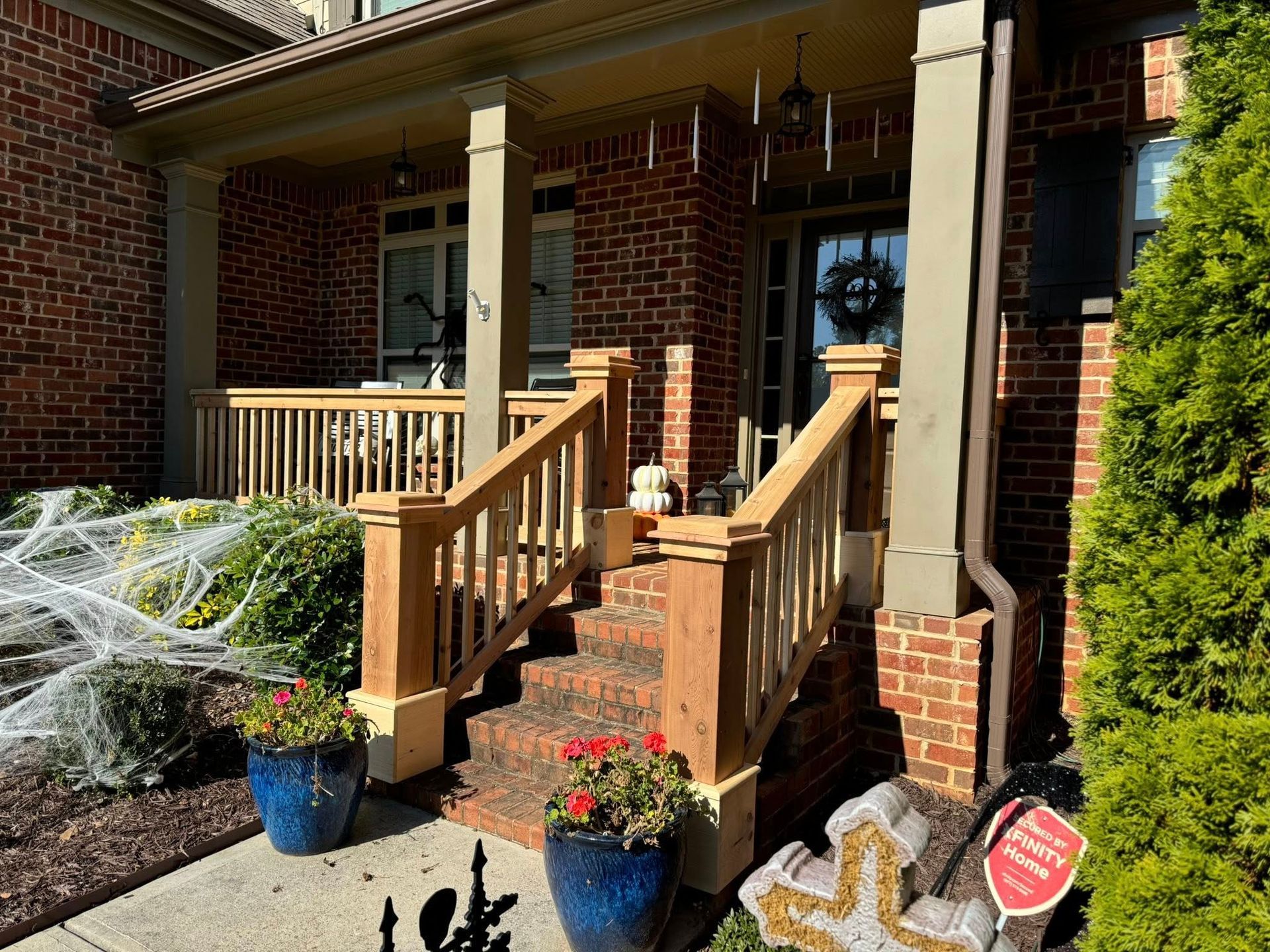 Halloween-decorated house with brick facade, porch, steps, and spider webs; fall decorations; front entrance.
