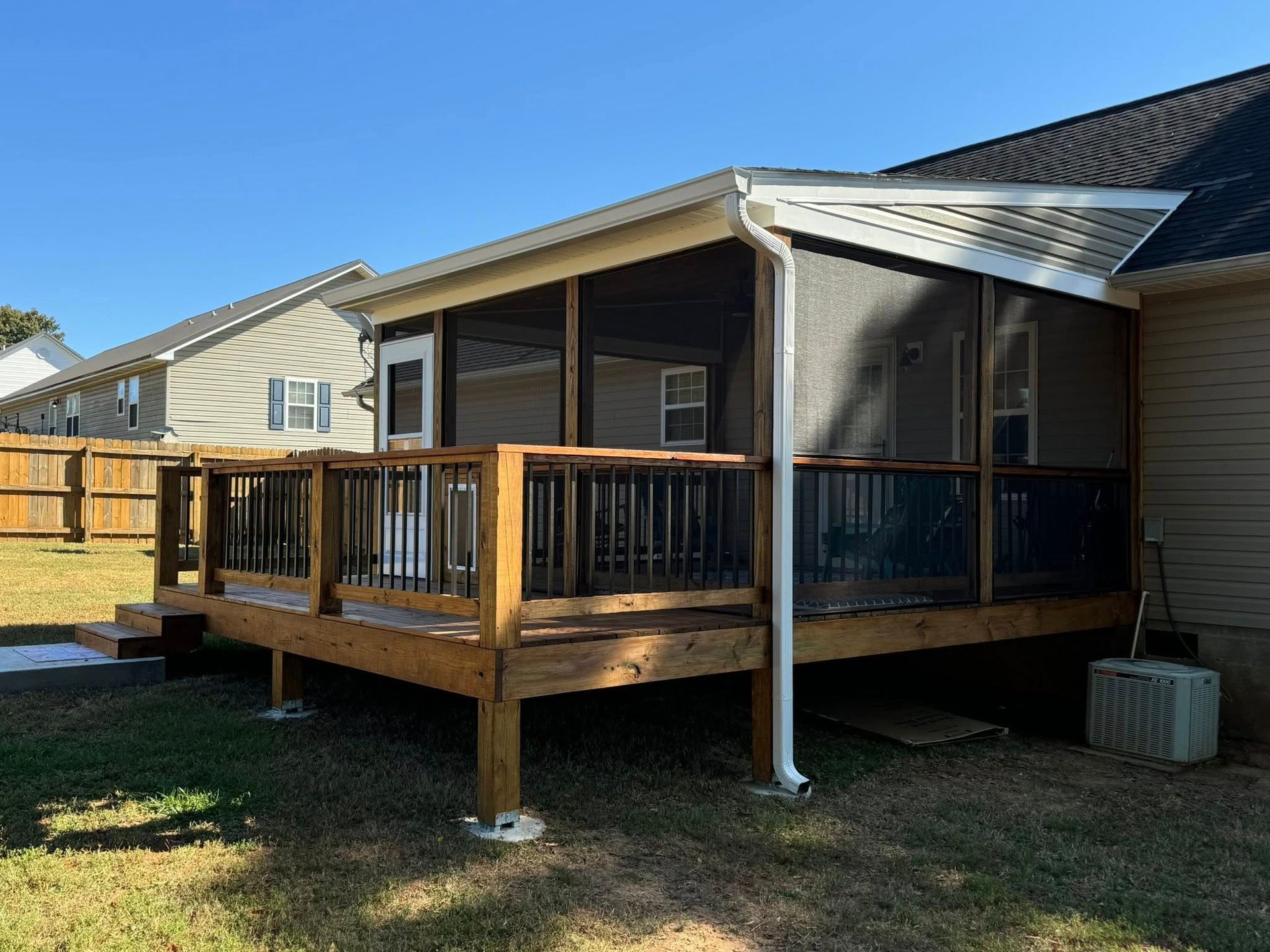 Wooden deck and screened-in porch on a house, surrounded by green grass, blue sky.