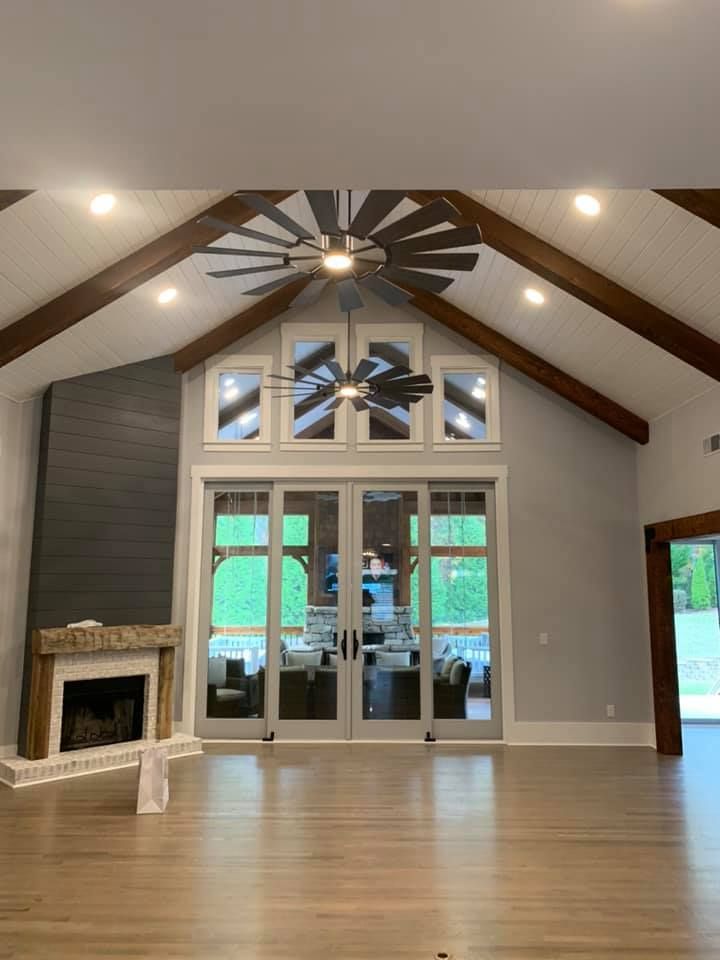 Spacious living room with a high, wood-beamed ceiling, fireplace, and large glass doors leading outside.