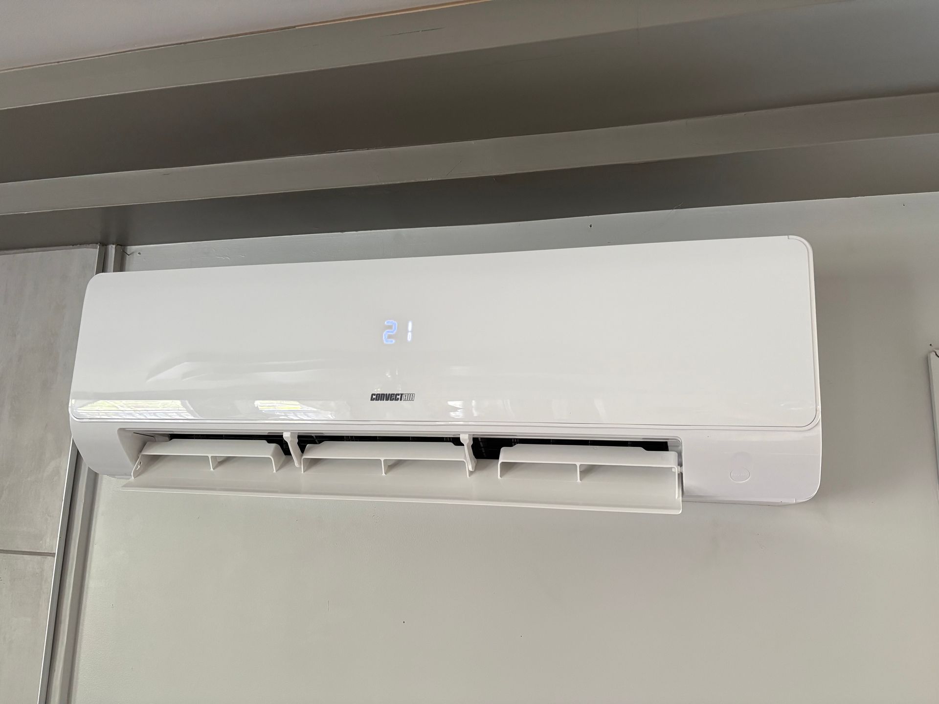 Un climatiseur mural blanc avec affichage numérique de la température, installé sur un mur clair.