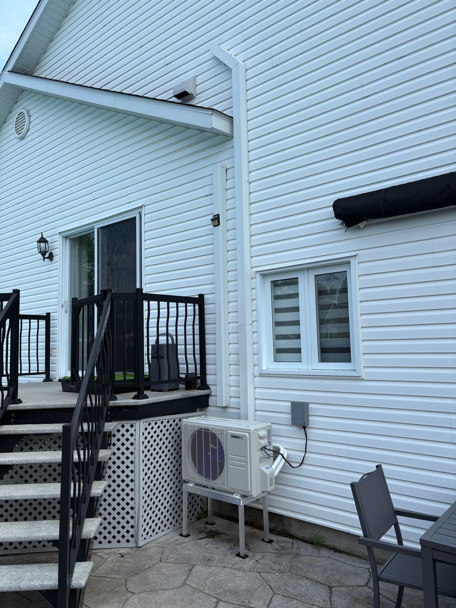 Revêtement extérieur blanc avec patio, escalier, fenêtre et unité extérieure de climatisation mini-split murale sur support.