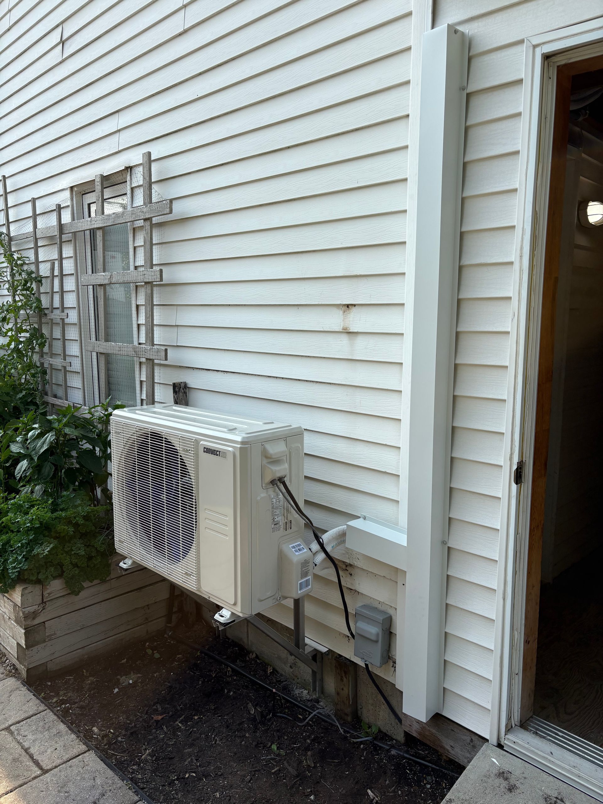 Un climatiseur mural extérieur installé sur le côté d'une maison blanche, à côté d'une porte.