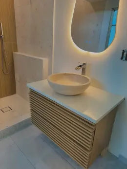 Bathroom with light wood vanity, stone sink, and backlit mirror. Shower to the left.